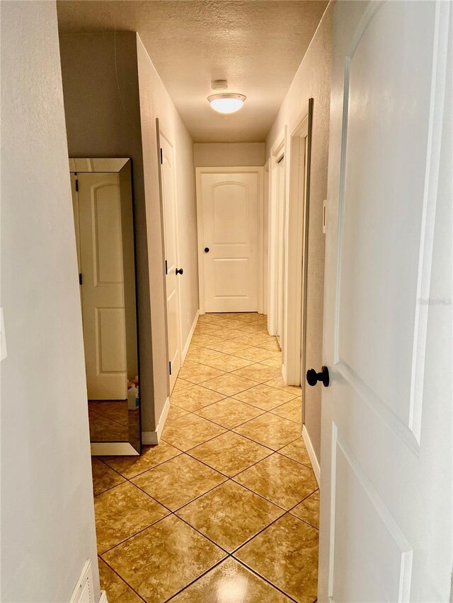 hall with a textured ceiling, light tile patterned floors, and baseboards