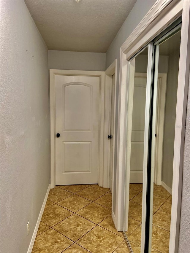 corridor featuring light tile patterned floors, baseboards, a textured wall, and a textured ceiling