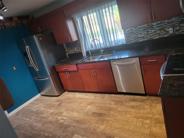 kitchen with light wood-type flooring, dark stone countertops, a sink, stainless steel appliances, and decorative backsplash