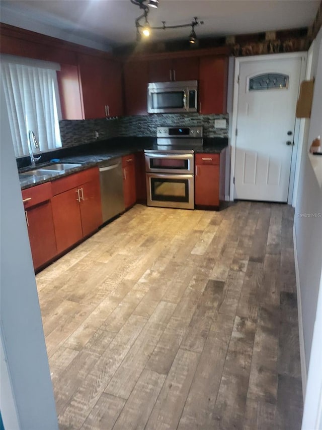kitchen featuring tasteful backsplash, light wood-type flooring, dark countertops, a sink, and stainless steel appliances