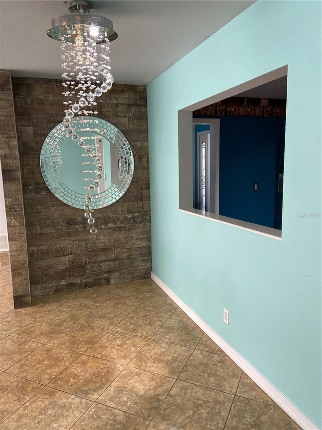 interior space with a chandelier, an accent wall, and baseboards