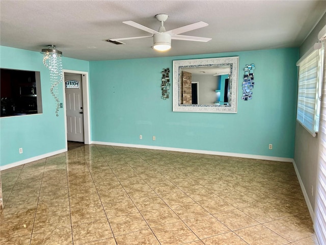 tiled empty room featuring visible vents, a textured ceiling, baseboards, and ceiling fan
