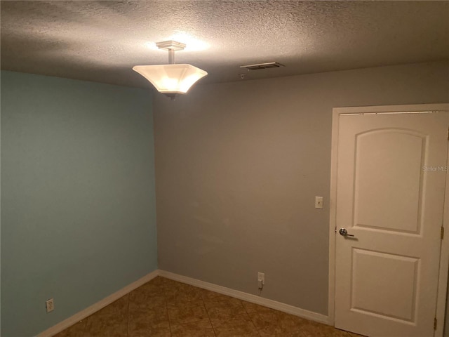 tiled spare room with visible vents, a textured ceiling, and baseboards