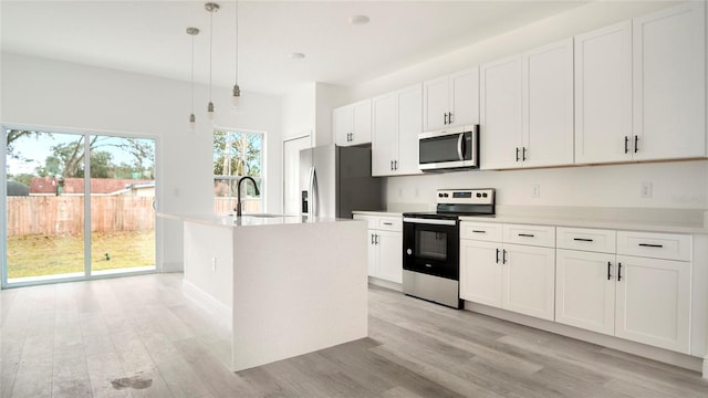 kitchen with pendant lighting, stainless steel appliances, white cabinets, and a center island with sink