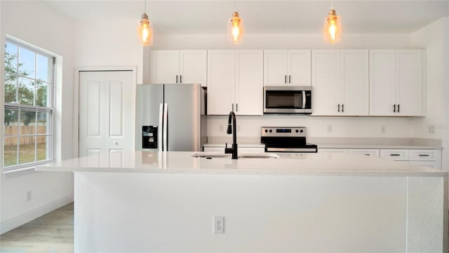 kitchen with an island with sink, decorative light fixtures, stainless steel appliances, and white cabinets