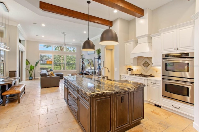 kitchen featuring white cabinetry, beamed ceiling, stainless steel appliances, decorative light fixtures, and sink