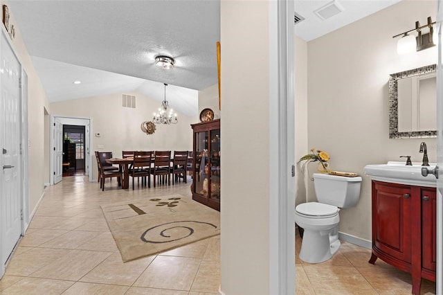 bathroom with a chandelier, vaulted ceiling, toilet, vanity, and tile patterned floors