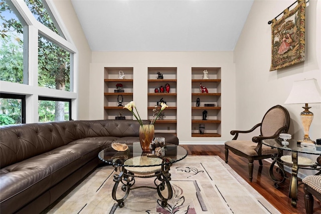 living room with built in features, wood-type flooring, and vaulted ceiling