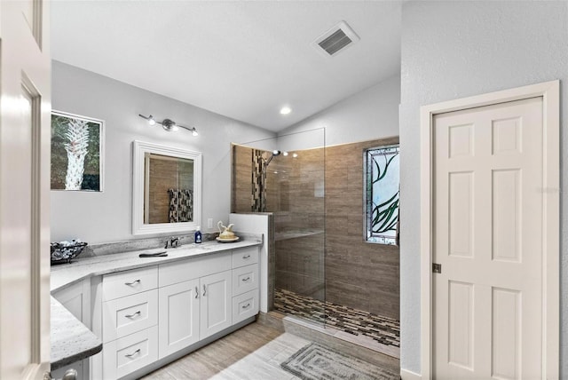 bathroom featuring vanity, lofted ceiling, wood-type flooring, and tiled shower