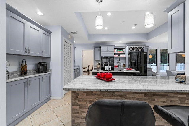 kitchen featuring a breakfast bar, black appliances, hanging light fixtures, and light stone counters