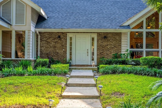 entrance to property featuring brick siding, a lawn, and a shingled roof