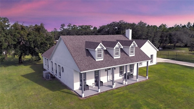 back house at dusk with a patio area, central AC, and a lawn