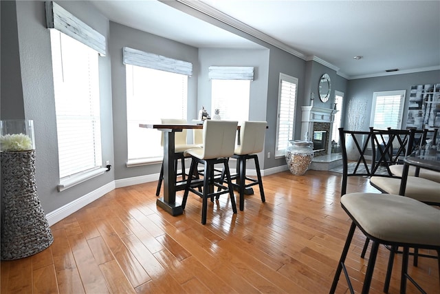 dining area featuring a healthy amount of sunlight, hardwood / wood-style flooring, a premium fireplace, and ornamental molding