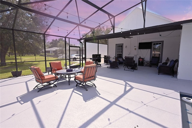 patio terrace at dusk featuring ceiling fan, a lanai, and a lawn