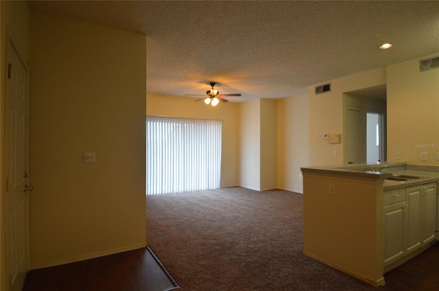 interior space featuring ceiling fan, sink, dark colored carpet, and kitchen peninsula