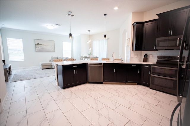 kitchen with appliances with stainless steel finishes, decorative backsplash, kitchen peninsula, pendant lighting, and sink