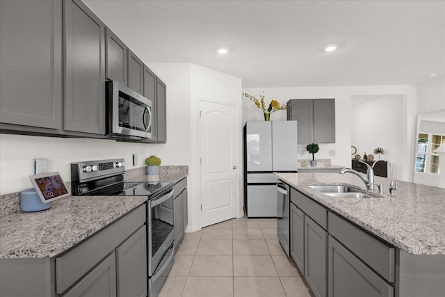 kitchen with a kitchen island with sink, light tile patterned flooring, sink, gray cabinetry, and appliances with stainless steel finishes