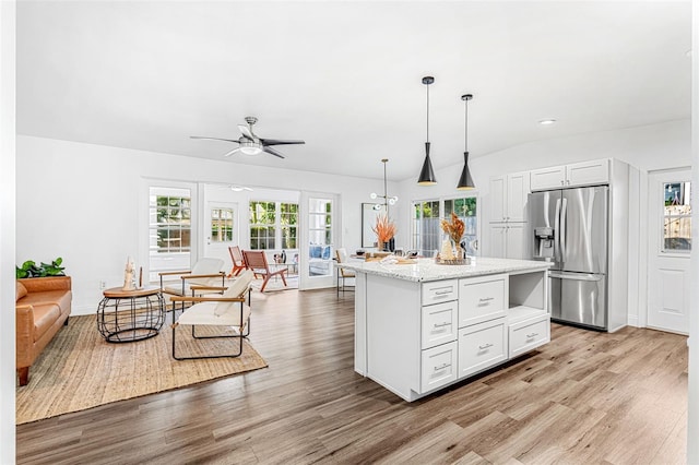 kitchen with white cabinets, stainless steel fridge with ice dispenser, light stone countertops, a center island with sink, and pendant lighting