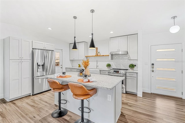 kitchen with light stone countertops, hanging light fixtures, a kitchen island, a breakfast bar area, and appliances with stainless steel finishes