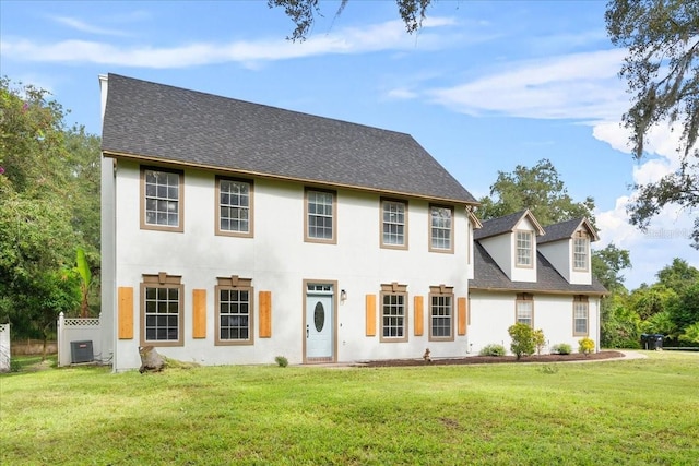 colonial home featuring a shingled roof, stucco siding, central AC unit, and a front lawn