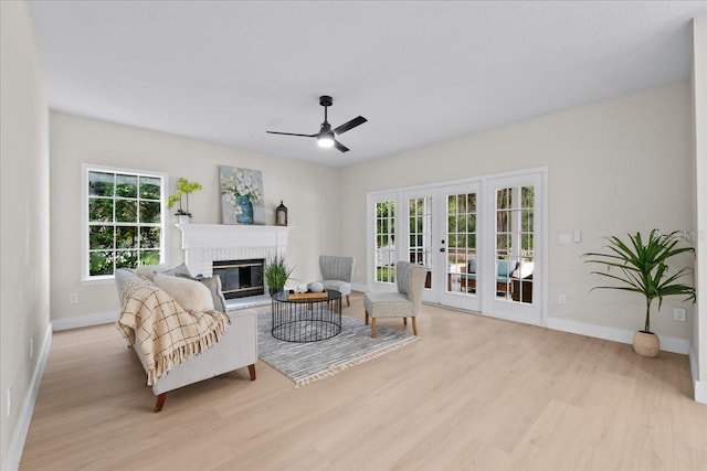 living room with light wood-type flooring, a fireplace, ceiling fan, and french doors