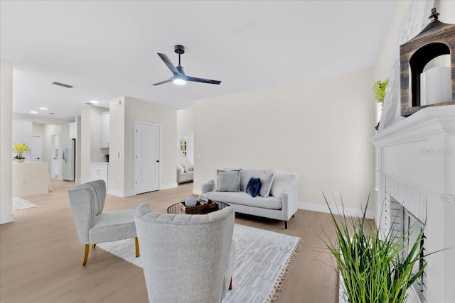 living room with a brick fireplace, light hardwood / wood-style floors, and ceiling fan