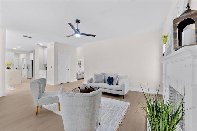 living room with visible vents, ceiling fan, light wood-style floors, and a fireplace