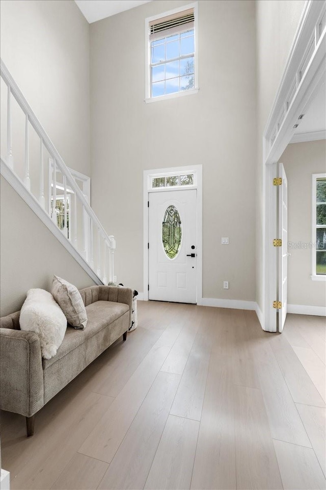 entryway with light wood-type flooring, a towering ceiling, and stairs