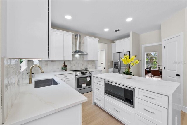 kitchen featuring wall chimney range hood, light hardwood / wood-style floors, sink, white cabinets, and appliances with stainless steel finishes