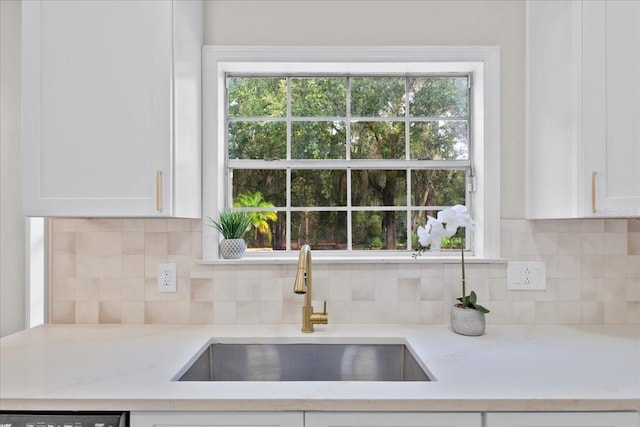 kitchen featuring light stone countertops, sink, a healthy amount of sunlight, and white cabinetry