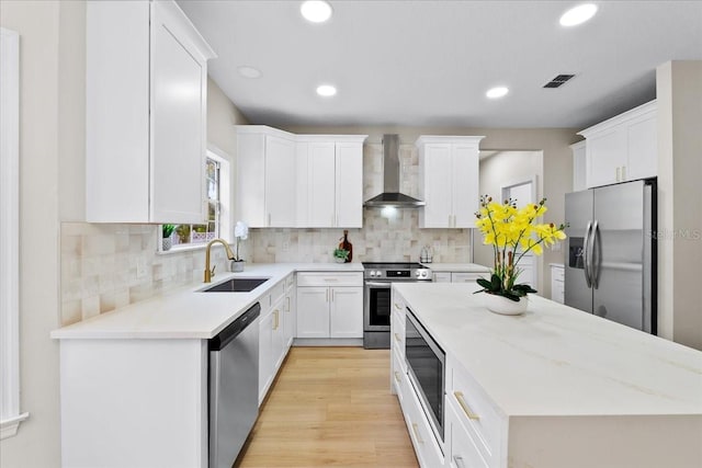 kitchen with wall chimney range hood, a kitchen island, visible vents, stainless steel appliances, and a sink