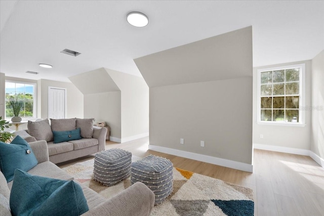living area featuring light wood-style floors, baseboards, vaulted ceiling, and visible vents