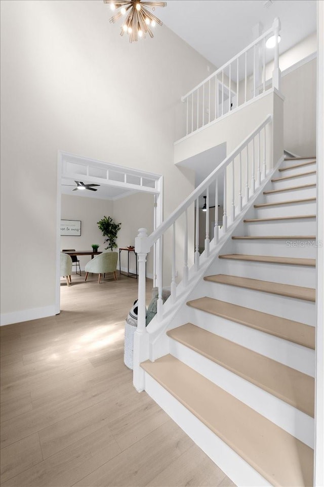 staircase featuring a towering ceiling, baseboards, an inviting chandelier, and wood finished floors