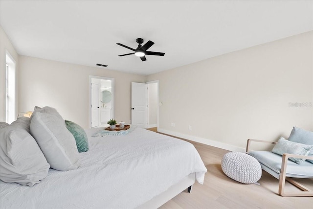 bedroom featuring baseboards, ensuite bath, a ceiling fan, visible vents, and wood finished floors