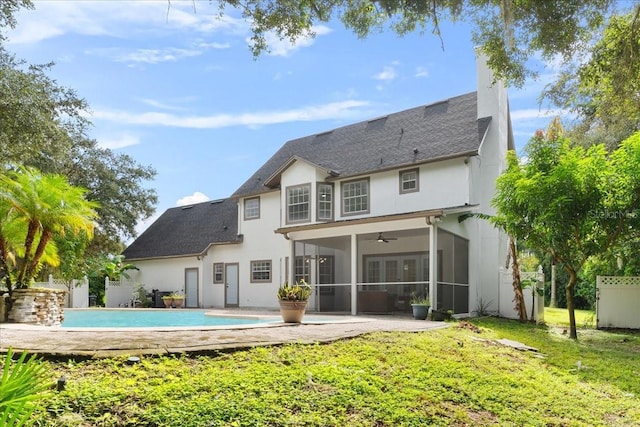 rear view of house with stucco siding, an outdoor pool, a sunroom, fence, and a lawn