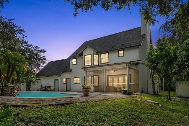 back of property at dusk with stucco siding, a chimney, an outdoor pool, a sunroom, and fence