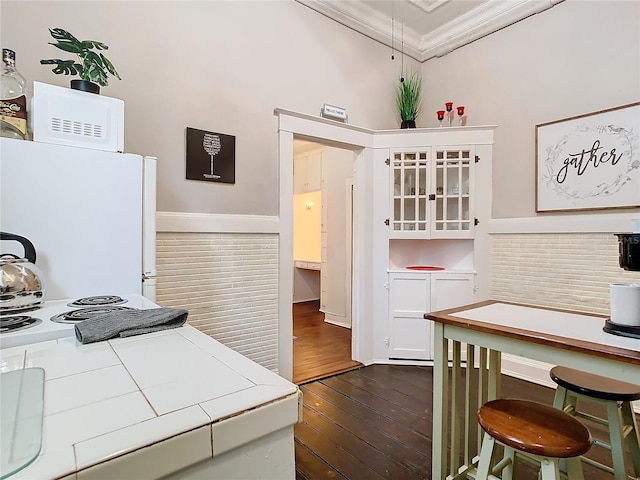 kitchen with tile countertops, white cabinets, white refrigerator, ornamental molding, and dark hardwood / wood-style flooring