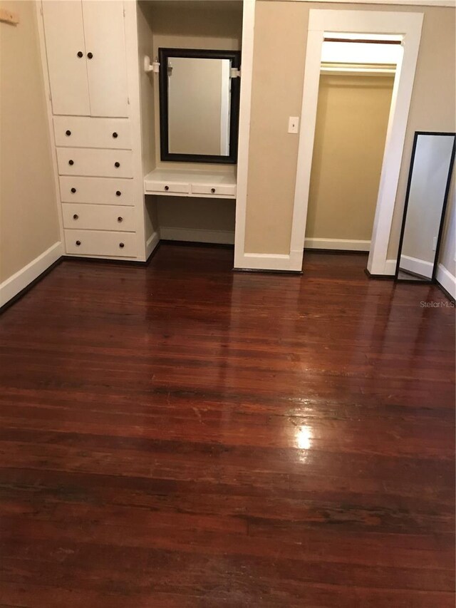 unfurnished bedroom with built in desk and dark wood-type flooring