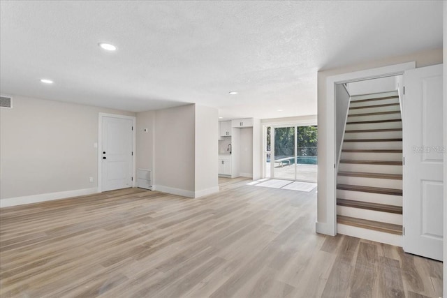 unfurnished living room with light wood finished floors, stairs, baseboards, and a textured ceiling