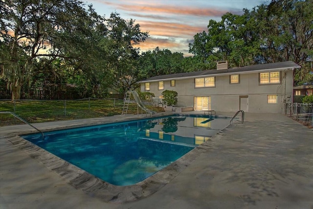 pool at dusk with a patio, a water slide, fence, and a fenced in pool