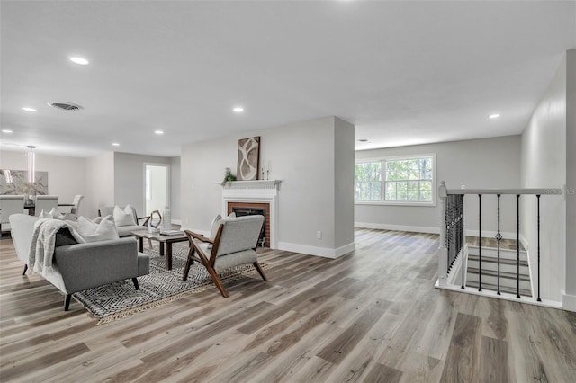 living area featuring recessed lighting, wood finished floors, visible vents, baseboards, and a brick fireplace