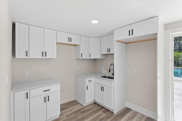 kitchen with light wood finished floors, white cabinetry, light countertops, and a sink