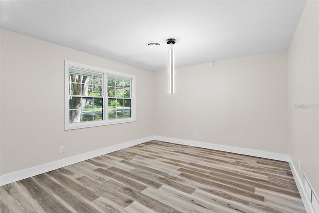 empty room featuring wood finished floors, visible vents, and baseboards