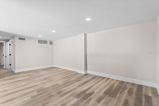 finished below grade area with light wood-style flooring, visible vents, and baseboards