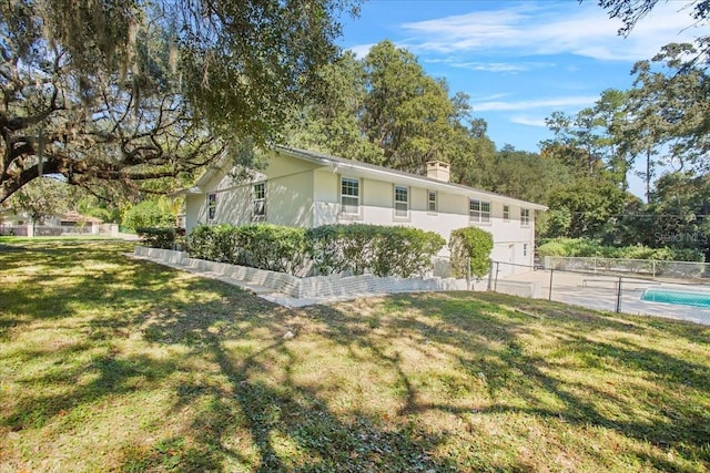 view of side of home featuring a fenced in pool, a chimney, stucco siding, a lawn, and fence