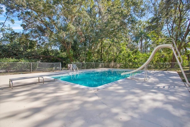 view of pool featuring a water slide, fence, a diving board, a fenced in pool, and a patio area