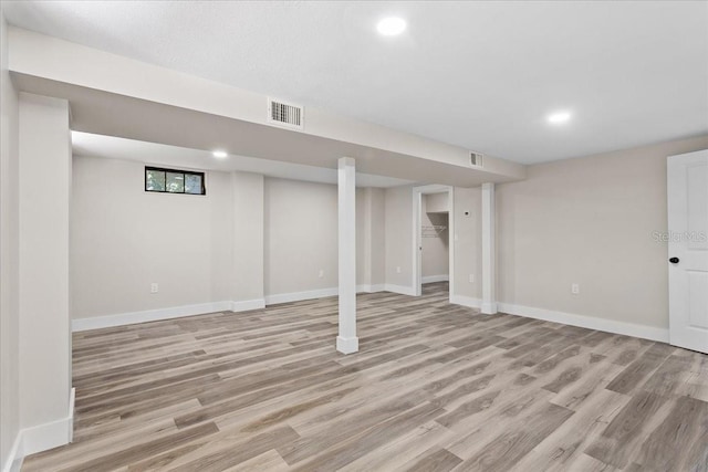 finished basement with baseboards, visible vents, and light wood finished floors