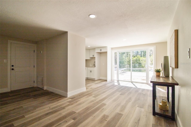 unfurnished living room with recessed lighting, light wood-style flooring, a sink, a textured ceiling, and baseboards