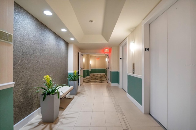 corridor featuring a tray ceiling, light tile patterned floors, and elevator