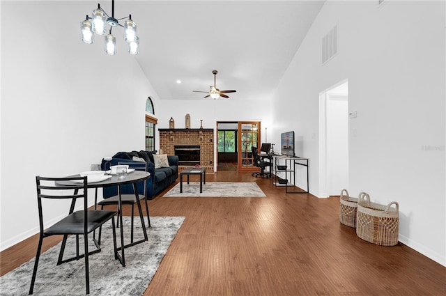 dining space featuring wood-type flooring, ceiling fan with notable chandelier, a fireplace, and high vaulted ceiling